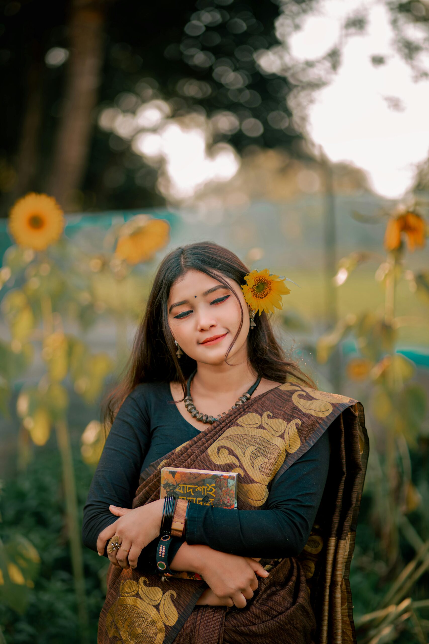South Asian woman in a sari posing with sunflowers in an outdoor setting.
